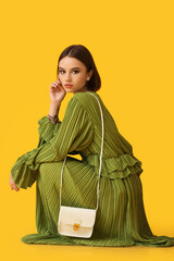 Young woman with stylish accessories squatting on color background