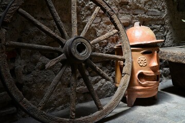 Rustic Wheel with terracotta planter with face near a stone wall with low light