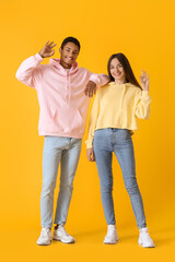 Fototapeta premium Stylish young couple in hoodies showing OK on yellow background