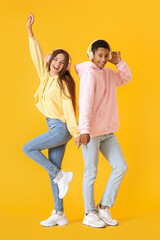 Fototapeta premium Stylish young couple in hoodies listening to music on yellow background