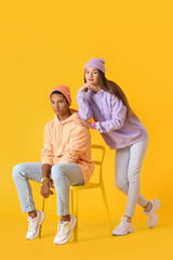 Stylish young couple in hoodies on yellow background