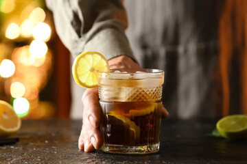 Male bartender with glass of tasty Cuba Libre cocktail on table in bar