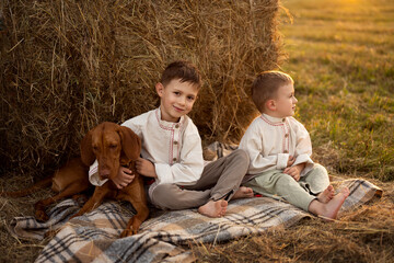 two boys sit near a haystack at sunset