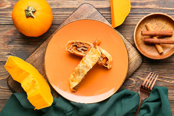 Plate with pieces of tasty pumpkin strudel and cinnamon on wooden background