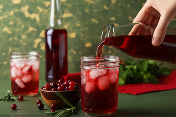 Woman pouring healthy cranberry juice from bottle into glass on color wooden background