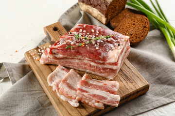 Wooden board with uncooked bacon on white background