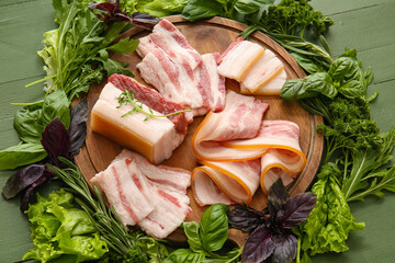 Board with uncooked and smoked bacon on green wooden background