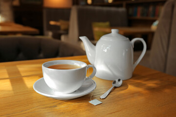 Cup of hot tea and pot on wooden table in cafe