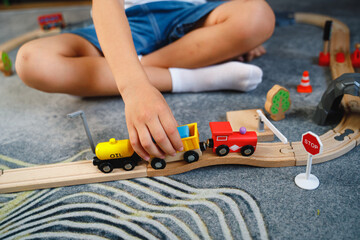 The boy is playing on the toy wooden road. Top view. Child boy playing in his room with a toy train.