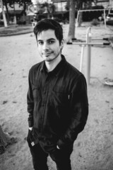 Handsome, young and happy caucasian guy with shirt standing and smiling in a park in the afternoon (in black and white)