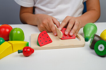 The child plays with wooden colorful toys. The child is cutting a wooden Watermelon for fruit...