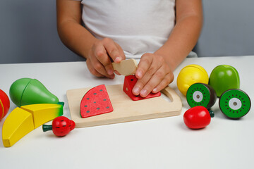 The child plays with wooden colorful toys. The child is cutting a wooden Watermelon for fruit salad. Educational logic toys for kid's. Children's hands close-up. Montessori Games for Child Development