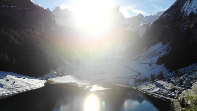 Aerial flyover over lake Seealpsee in Appenzell, Switzerland with winter snow and sunshine