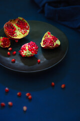 Overhead shot of a plate  fresh pomegranate and seeds on dark blue background .