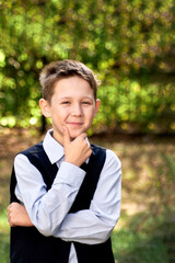 Portrait of a schoolboy looking thoughtfully to the side, against a blurry background of green trees.