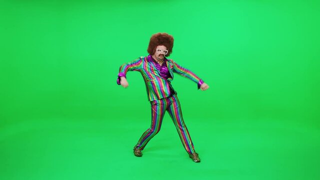 A retro dude in a multicolored suit is dancing a funny dance on a green background, a festive mood, a retro disco man is having fun at a new year's party.