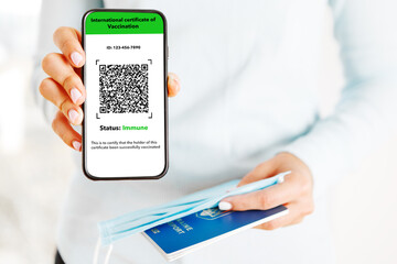 The woman holding the mobile phone a mockup for digital vaccination certificate in one hand and passport, mask and ticket in another one