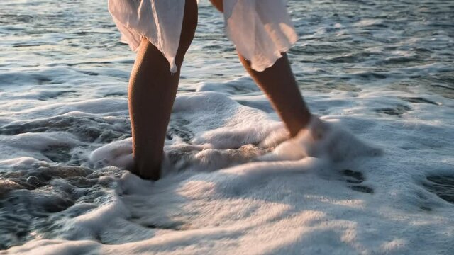 The surf, a wave with foam washes the woman's feet.