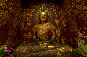 An ancient monumental Buddha statue sitting in meditation posture is covered with gold leaf.