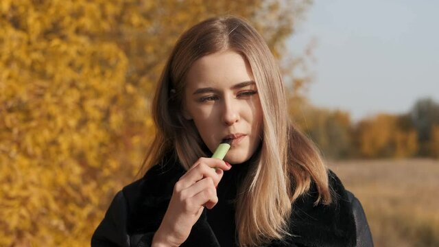 Cute girl smokes electronic and smiles. Close-up. Autumn.