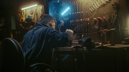 Fototapeta premium Young blacksmith man with workwear, taking solder tool, sitting on chair and do solder.