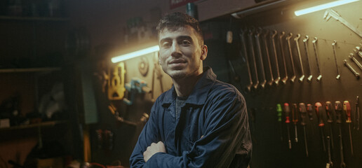 Young blacksmith man with workwear fold one's arms, looking at camera and smiling