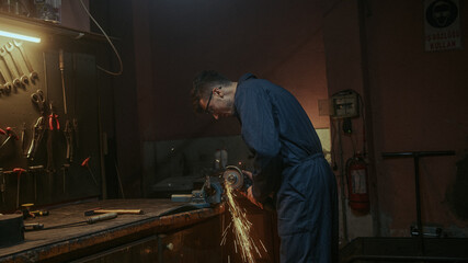 Young blacksmith man use iron or metal cutting machine and he metal grinding on steel spare part in...