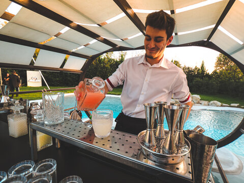 Bartender Mixing Drinks Outdoors Near A Pool At Sunset