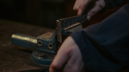 Close-up at part of a rustic old metal grip clamp, young blacksmith clamps the metal or iron part...