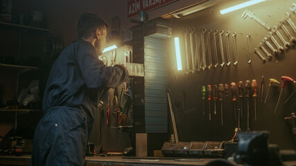 Male young blacksmith man putting his tools and equipment in place in his awesome looking workshop, back view