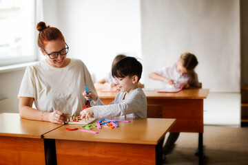 teacher and the student at the school desk collect letters with a simulator, the teacher explains and deals with the boy in the lesson, individual work. Light class, real class in private school