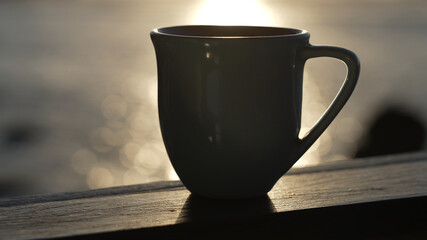 large blue mug with a drink standing on a wooden side against the background of the ocean. Close-up of a mug against water with solar glare. Slow motion.