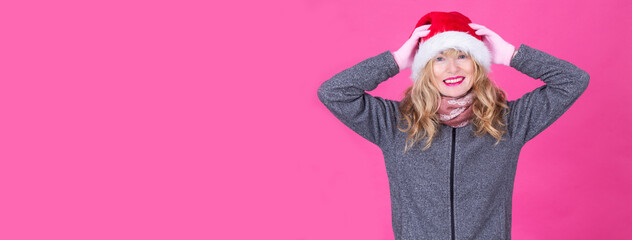smiling woman wearing santa claus hat on pink background. holiday celebration concept
