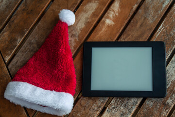 Obraz na płótnie Canvas digital tablet with santa claus hat on wooden background