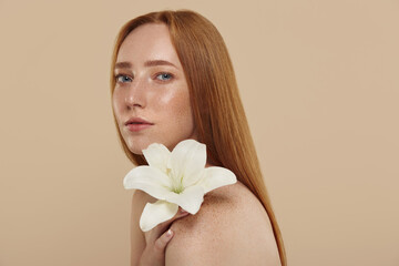 Obraz na płótnie Canvas Redhead girl with naked shoulders hold lily flower