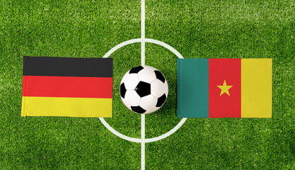 Top view soccer ball with Germany vs. Cameroon flags match on green football field.