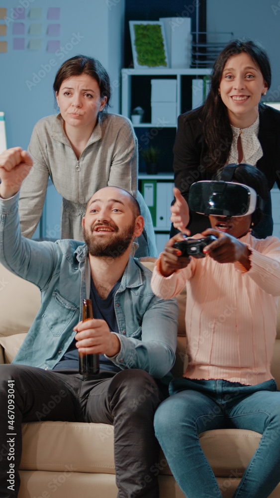 Wall mural African american woman using vr glasses and controller to play video games while colleagues cheering for entertainment after work. Coworkers playing with technology to do fun activity