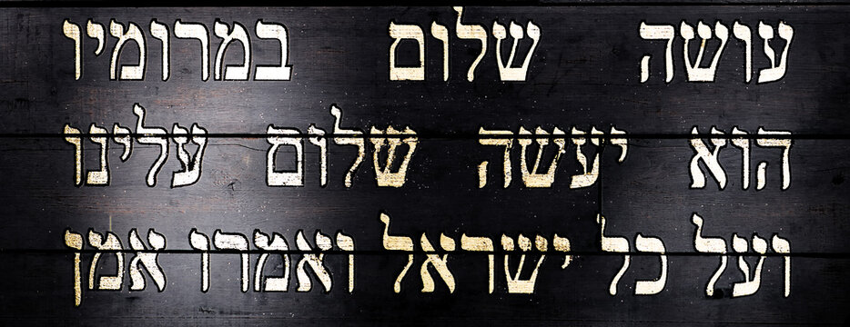 Last lines of Jewish prayer Kaddish on black wooden background. Translation is: He who creates peace in His celestial heights, may He create peace for us and for all Israel, and say, Amen.