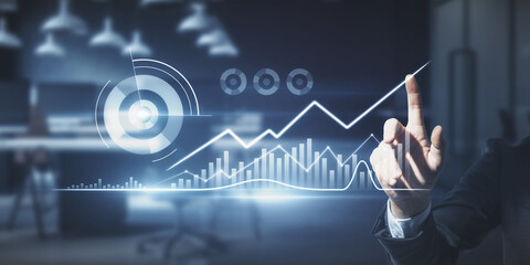 Close up of businessman hand pointing at abstract glowing business chart on blurry office background. Finance and innovation concept. Double exposure.