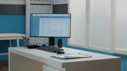 Close up of computer screen with patient information on desk in empty medical cabinet. Nobody in doctors office with healthcare equipment and instruments for consultation and examination
