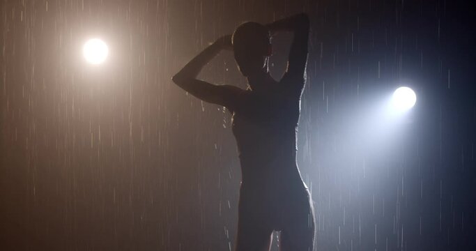 Fit Lady in Aqua Studio in swimsuit. Athletic build,attractive figure in foggy rainy studio, attractive lady silhouette enjoys rain, feeling free and sexy, moving tenderly, light in the background.