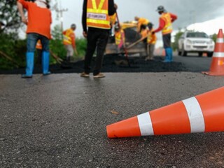 Blurred image of road maintenance work in Asia and there is an orange cone in front.