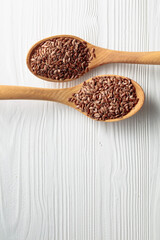 Wooden spoons with flaxseed on a white wooden table.