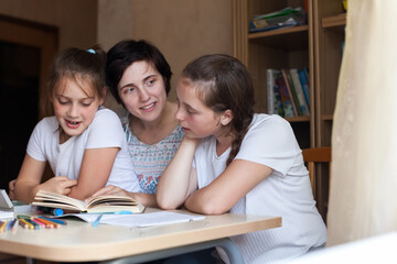 Fototapeta premium Enthusiastic children read book at table with their mother