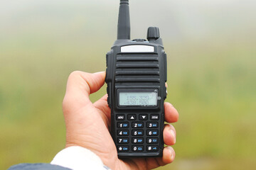 Black walkie talkie in a hand, mountains on the background.