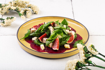 beet carpaccio with spinach and feta on white tile background with flowers