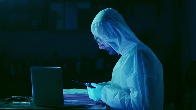 Forensic investigator making list of crime evidence in dark basement with blue lights