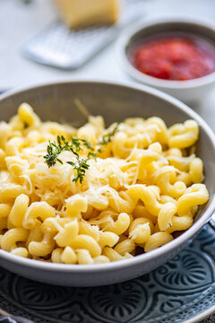Bowl of cavatappi pasta with grated parmesan cheese and a bowl of tomato sauce