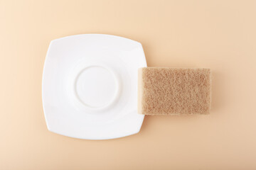 Dishwashing minimal creative concept in light beige colors. White ceramic plate and cleaning sponge top view