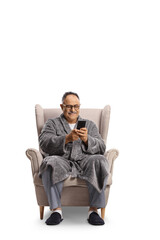 SMiling mature man in a bathrobe sitting in an armchair and typing on a smartphone